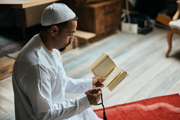 Middle Eastern man prays while reading from Koran and holding misbaha beads.