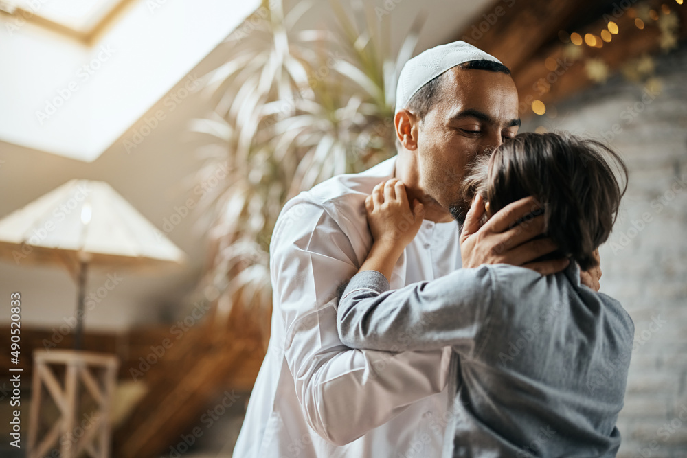 Wall mural caring muslim father kisses his daughter in forehead at home.