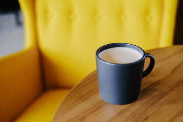 Cup of coffee on wooden table on a background of a yellow armchair