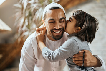 Affectionate Muslim girl kisses her father while embracing him at home.