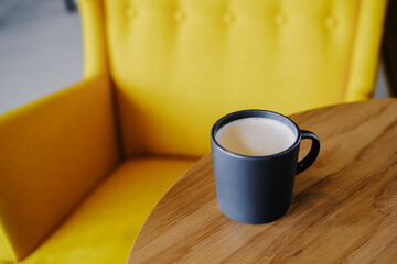 Cup of coffee on wooden table on a background of a yellow armchair