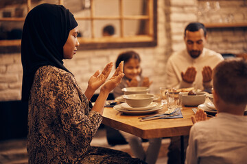 Muslim family prays together before a meal at dining table.