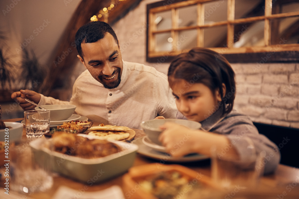 Wall mural happy muslim father talks to his daughter while having dinner at dining table.