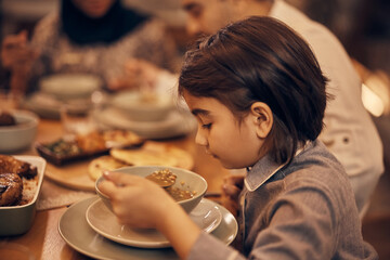 Little Muslim girl eats during evening family meal at home.