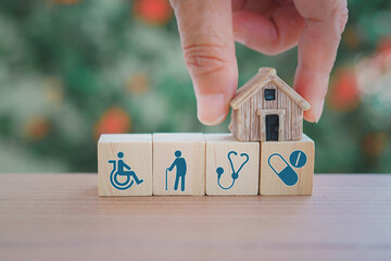 miniature house with blurred hand on row of wood cubes with elderly, disability person, stethoscope...