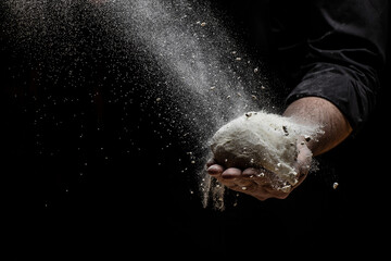 Fototapeta na wymiar Beautiful and strong men's hands knead the dough from which they will then make bread, pasta or pizza. A cloud of flour flies around like dust. Food concept.