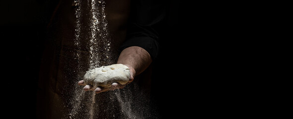 flying pizza dough with flour scattering in a freeze motion of a cloud of flour midair on black. Cook hands kneading dough. copy space
