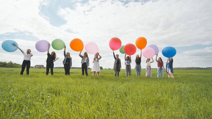 Cheerful girls are standing on the field with large balloons and colorful balloons.