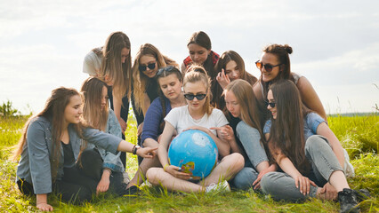 A group of cheerful girls is exploring the globe of the world in the meadow.