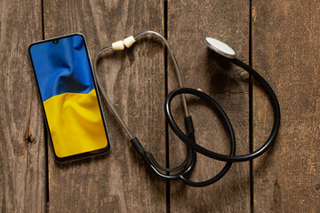 The stethoscope lies next to the phone and a photo of the national flag of Ukraine is yellow and blue. Doctors during the war, stop war 2022