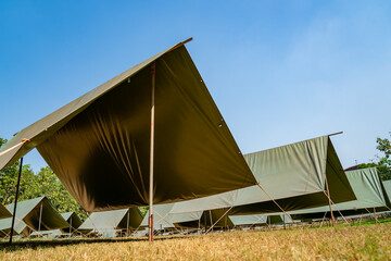 The simple and normal empty Canvas Tents in the row and column on the grass field at outdoor field in afternoon time.