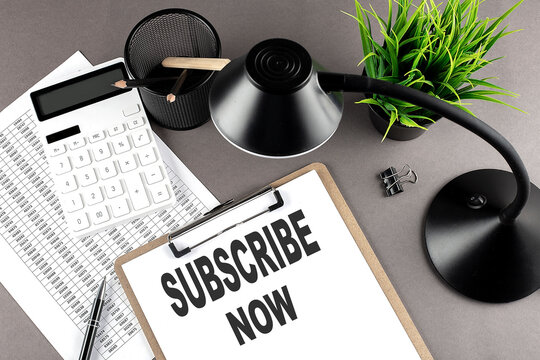 Clipboard ,chart and calculator, lamp and workspace accessories on a grey table. Top view , text SUBSCRIBE NOW