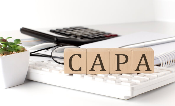 CAPA written on a wooden cube on keyboard with office tools