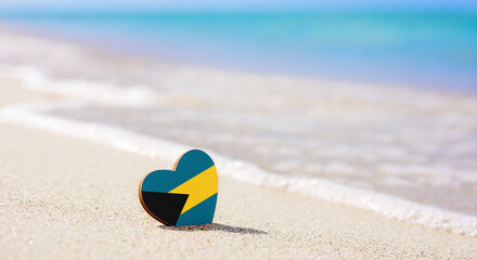 Flag of the Bahamas in the shape of a heart on a sandy beach. The concept of the best vacation in Bahamas