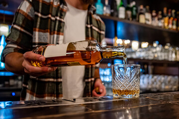 Barman pouring whiskey from bottle on glass in bar
