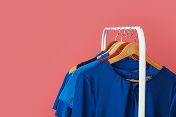Rack with clean blue clothes on pink background, closeup