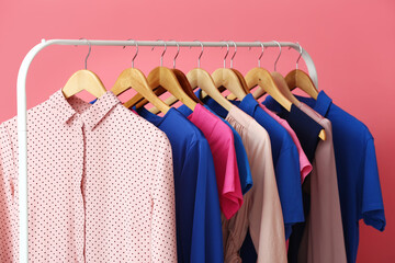 Rack with clean colorful clothes on pink background, closeup