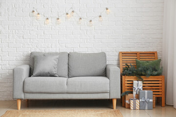 Fir branches in chest of drawers, Christmas gifts and sofa near white brick wall
