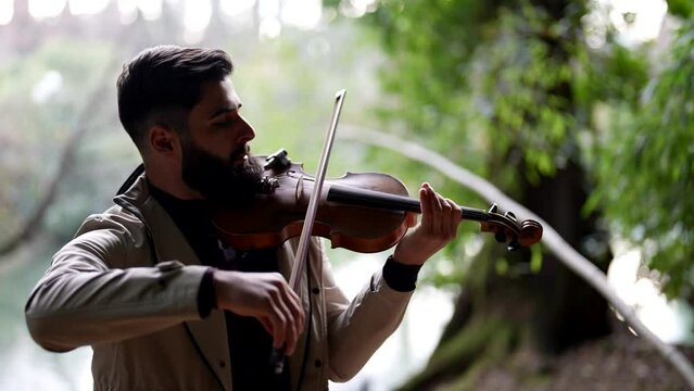 man is playing music by violin in forest with lake, concert of classical music in romantic place in nature