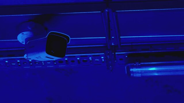 Security camera moving panning and tilting recording what's happening outside building . Night vision security camera hangs on roof inside parking or office near ventilation system . Security concept
