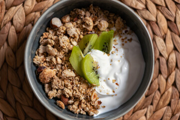 Roasted healthy homemade granola with Gluten Free Rolled oats or porridge oats, variety of chopped nuts and seeds and fresh kiwi pieces. Portion of granola and kefir or yogurt in bowl