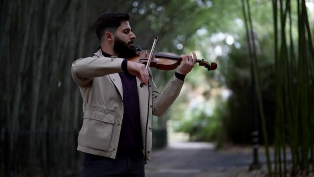 handsome man is playing violin in garden in summer, romantic musician play fiddle outdoor