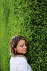 Young woman in white shirt with natural makeup standing by green hedge
