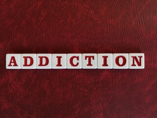 The word Addiction is spelled with white and red tiles on a red leather background sheet