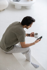 Young modern businessman with mobile phone sitting on white staircase in the morning and texting or scrolling through online news