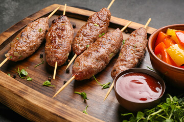 Wooden board of skewers with tasty lula kebab and sauce on table, closeup