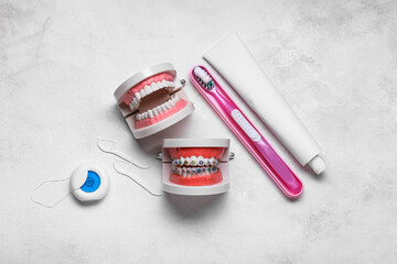 Model of jaws with braces, toothbrush, dental floss and paste on light background