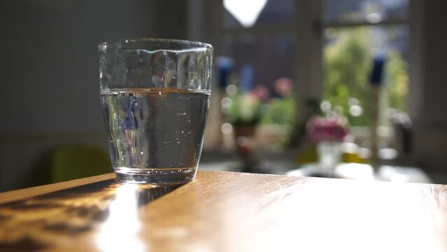 Slow pan around a glass of water in a sunny home with a garden visible in the background.