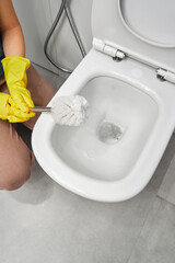 Woman's hand in yellow rubber gloves with a brush near the toilet.