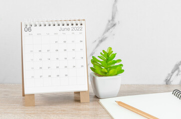 June 2022 desk calendar with plant on wooden table.