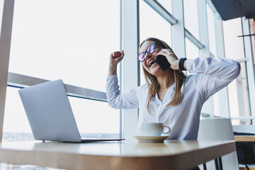 A young female manager in glasses works at a laptop and gesticulates emotionally with her hands...