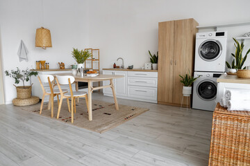 Interior of light kitchen with washing machines, dining table and cupboard