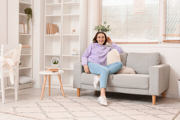 Happy young woman sitting on couch in room