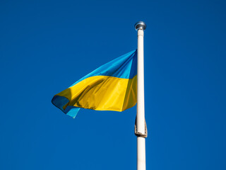 The blue and yellow Ukrainian flag flying in the sky on the flagpole in sunlight. The national flag of Ukraine has two equally sized horizontal bands of blue and yellow