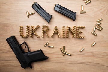 Napis ukraine ułożony z naboi na stole, wokół rozrzucone naboje, broń krótka oraz dwa załadowane magazynki