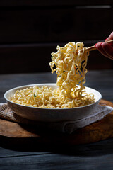 man takes a portion of hot noodles with chopsticks, dark background, vertical