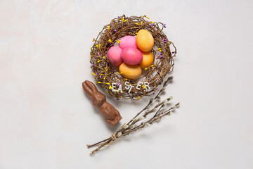 Obraz na płótnie Canvas Nest with colorful Easter eggs, chocolate bunny and pussy willow branches on light background
