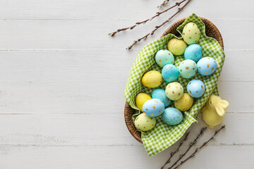 Basket with painted Easter eggs, willow branches and bunny on light wooden background