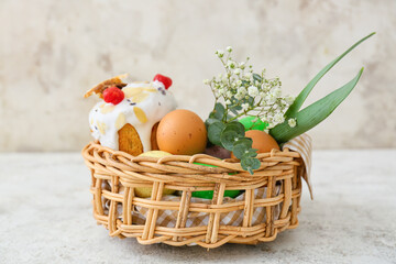 Gift basket with painted Easter eggs, flowers and cake on light background