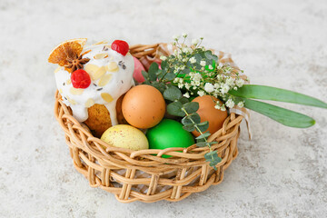 Gift basket with painted Easter eggs, flowers and cake on light background