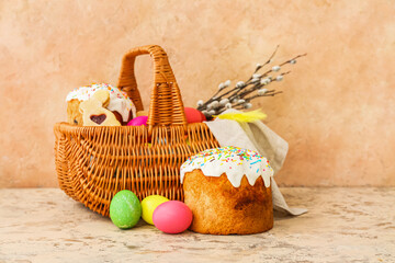 Fototapeta na wymiar Gift basket with painted Easter eggs and cakes on beige background