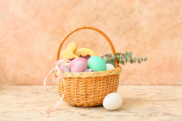 Gift basket with painted Easter eggs and cookies on beige background