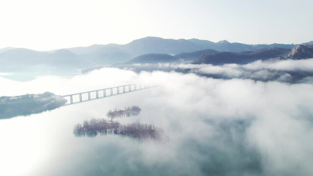 Aerial view of a lake covered in mist. Lake with foggy environment below a clear blue sky with no clouds in Le&oacute;n, Spain. Mountain range in the background and steel bridge across the clear lake water.