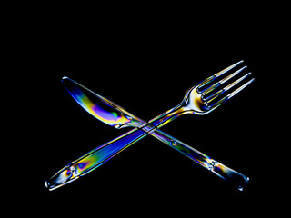 Bright rainbow stress patterns show in transparent plastic cutlery. Polarised light on a dark background.