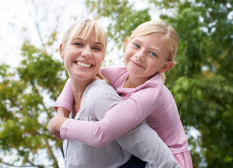 Wrapped in my daughters love. A happy young mother givign her daughter a piggyback ride in the park.