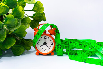 Measure tap with orange clock on white wooden background. Diet concept.